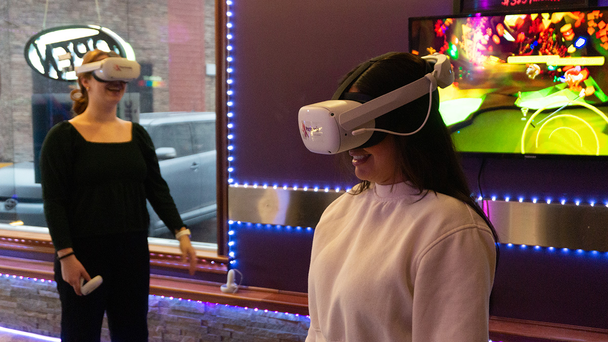 Two people play virtual reality. They are smiling and wearing headsets.
