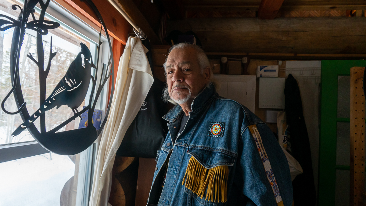 Albert looking out window Dumont in his home at Kitigan Zibi Anishinabeg First Nation with a blue jay sign.