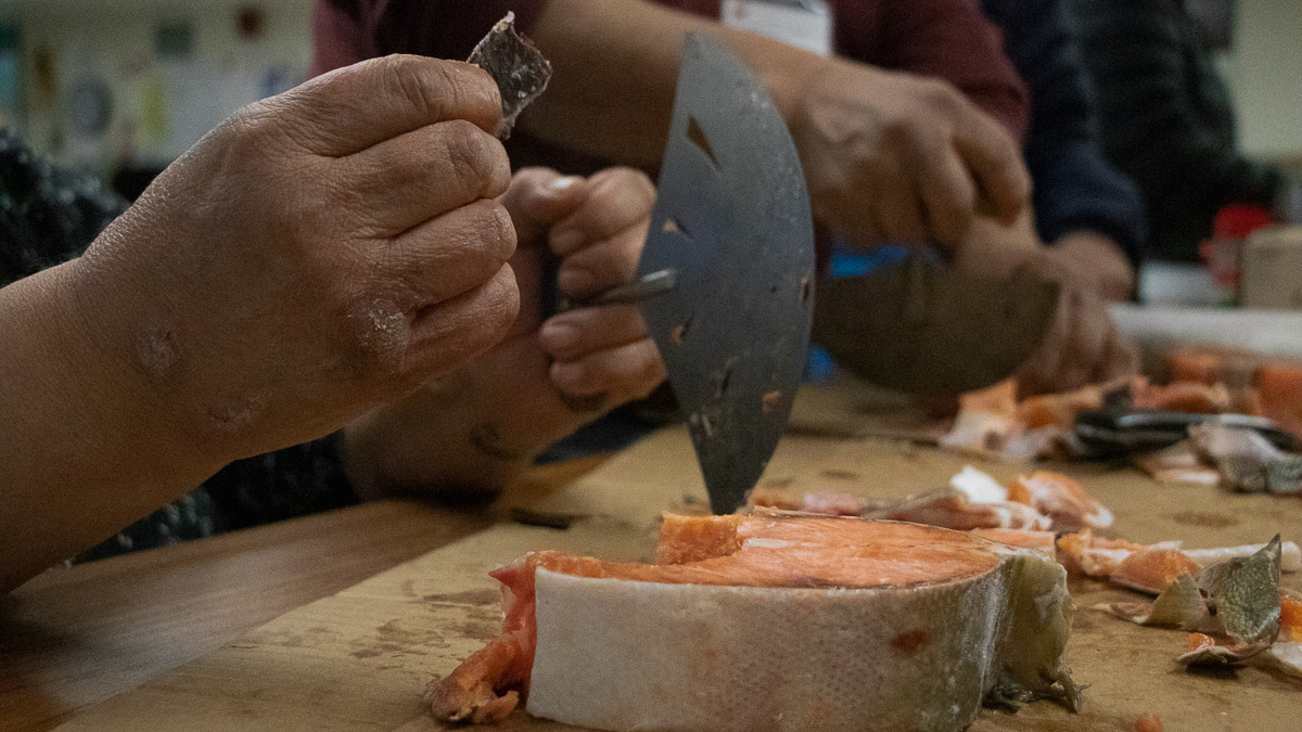Photo 5edit Woman holds a piece of arctic char in one hand and an ulu (knife) in the other.