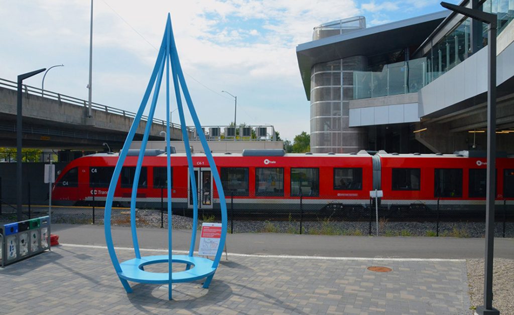 Blue statue by Pierre Poussin stands by the Line Two O-Train at Bayiew station.