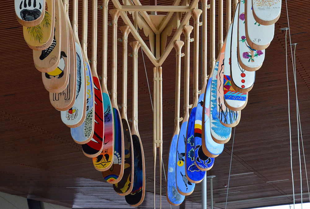 Algonquin Anishinabe hand-painted canoe paddles hang from the ceiling at Pimisi station.