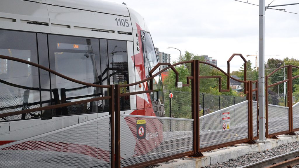 An eastbound LRT train waits behind the brown fence.