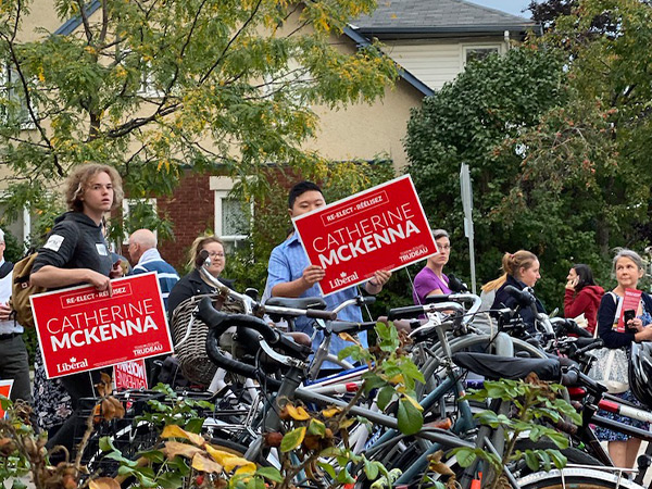 Two people outside hold up Catherine McKenna's street signs.