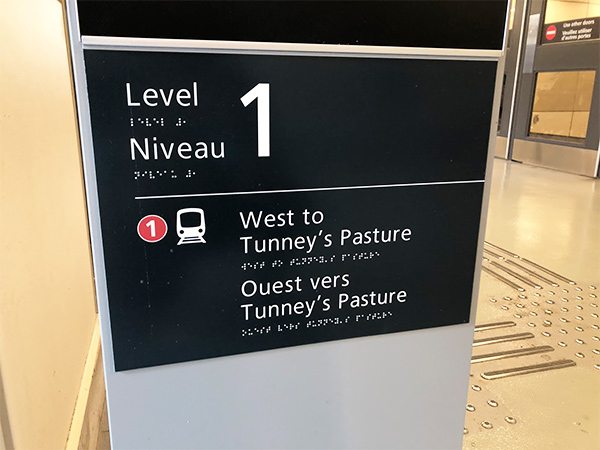 A sign is shown displaying tactile wayfinding details, notably raised text and Braille, and raised bumps on the station floor.