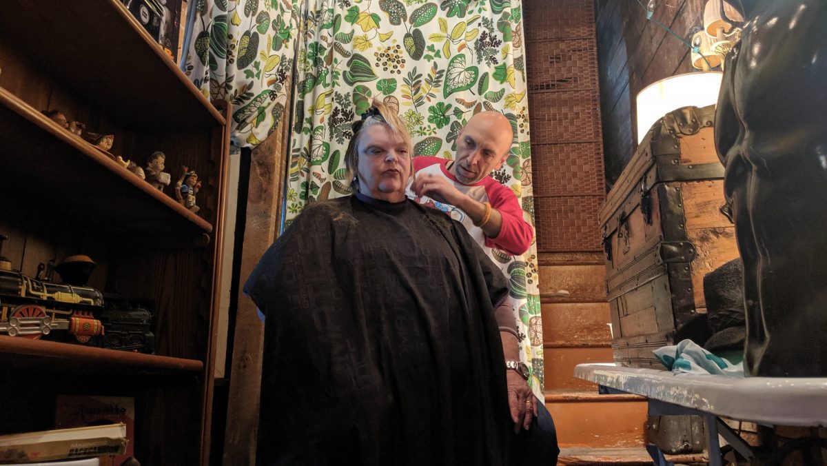 A man cuts a woman's hair in the corner of a small room. 