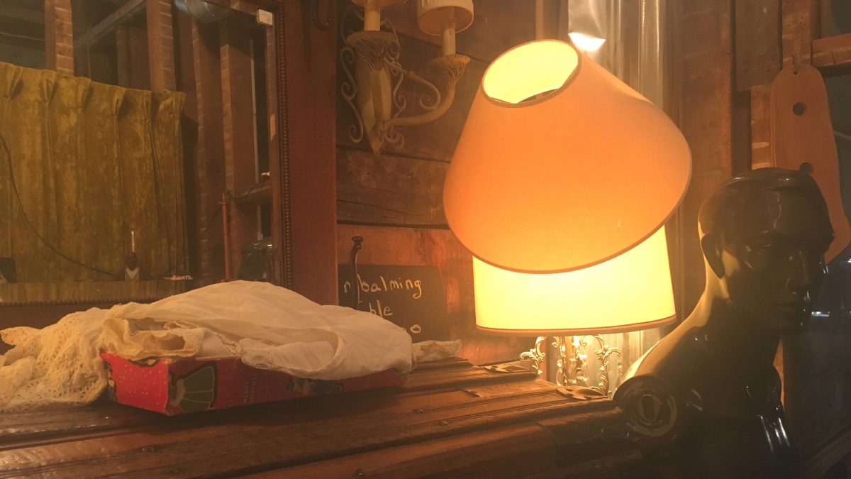 A lamp sits on top of a table beside a vintage manequin.