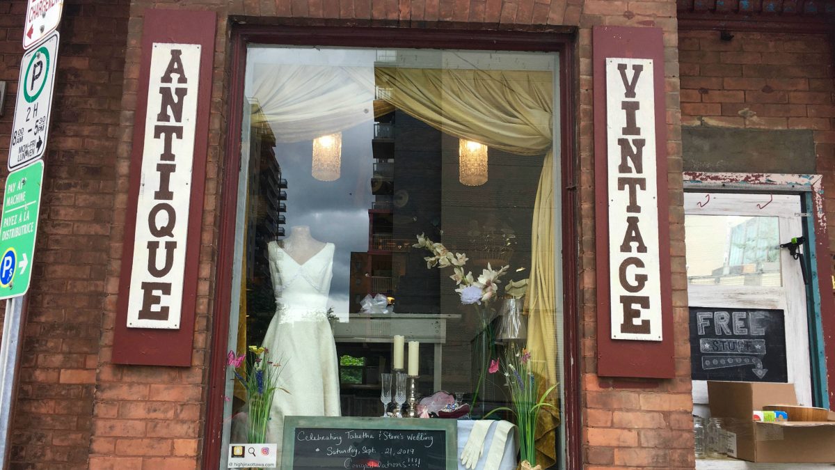 A window display in a red brick building. There is a mannequin wearing a wedding dress and a small chalkboard sign that says "Celebrating Tabatha and Steve's Wedding!"