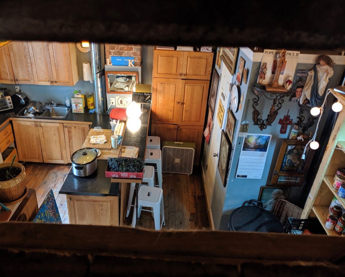 Framed between an open staircase is a small kitchen with many photos hanging on the wall.