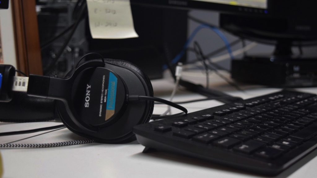 A pair of headphones sit next to a keyboard on a desk. 