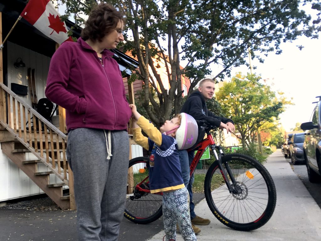 A young boy tugging on his mother's shirt accompanied by a teenager on his bike looking straight ahead.