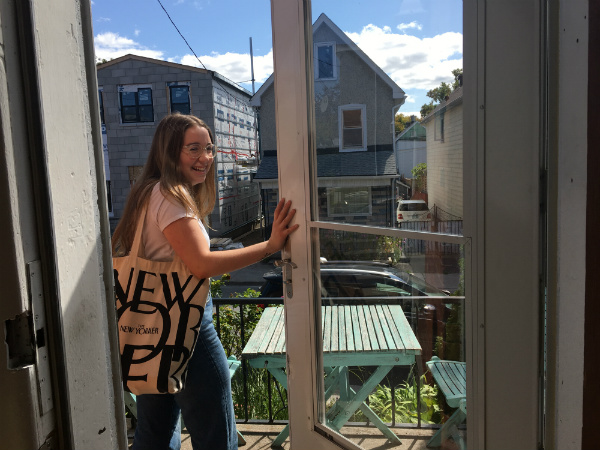 A girl exits a door, turns and smiles.