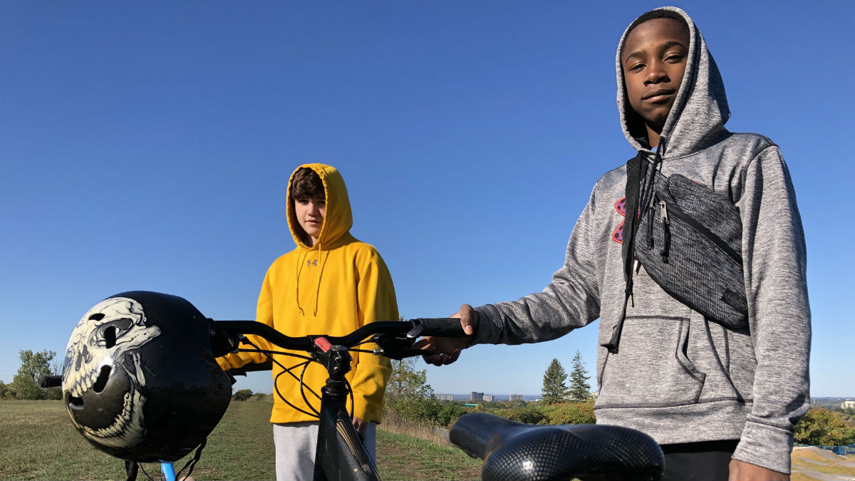 Two 13-year-old boys stand with their bikes overlooking a bike park.