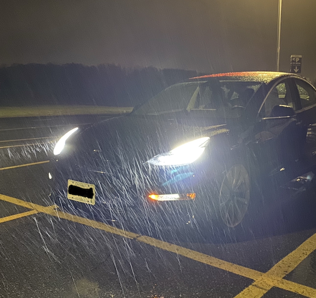 Picture of a Tesla with the headlights on in the rain.