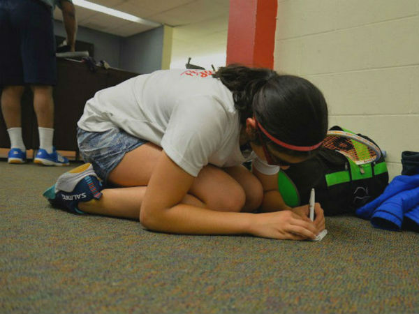 girl writes in notebook, crouched on carpeted floor.