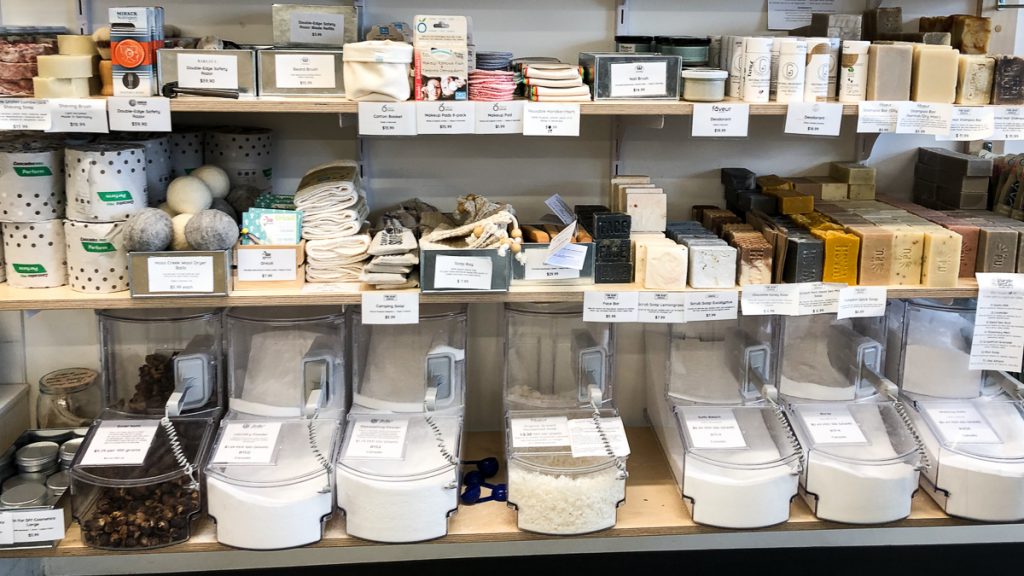 Three shelves of cleaning and personal hygiene products at NU Grocery, the bottom row of which is in bulk containers.