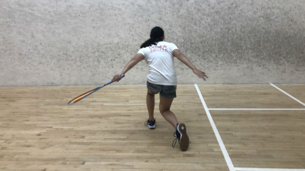 Arms outstretched, athlete in white t-shirt follows through on her shot.