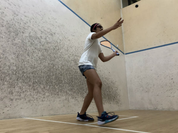 squash player serves, with the ball just above head height and racket ready to swing.