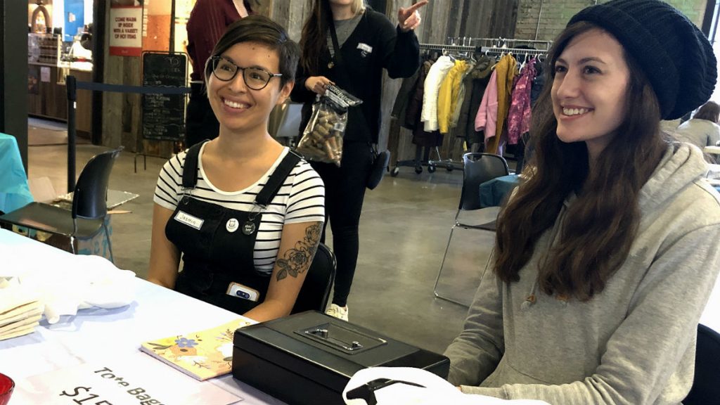 Jasmin Yee, left, and Taraneh Dohmer sit near the entrance of the event selling feminist-themed tote bags. 