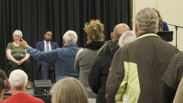 Panelists sit on stage as a line of residents ask their questions.