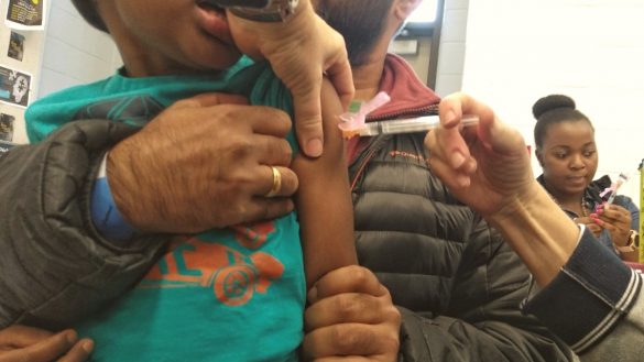 Child receiving injection while parent comforts them on their lap.
