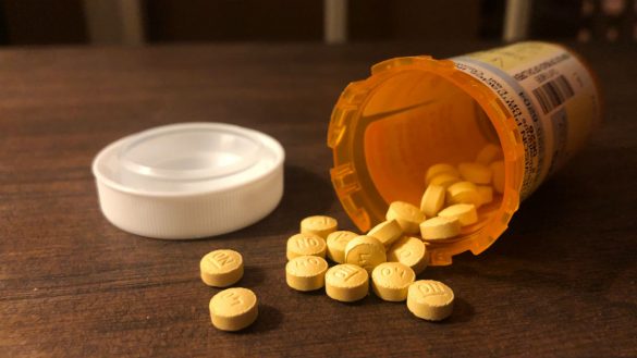 Opioid pills fall out of an orange pill bottle on a table.