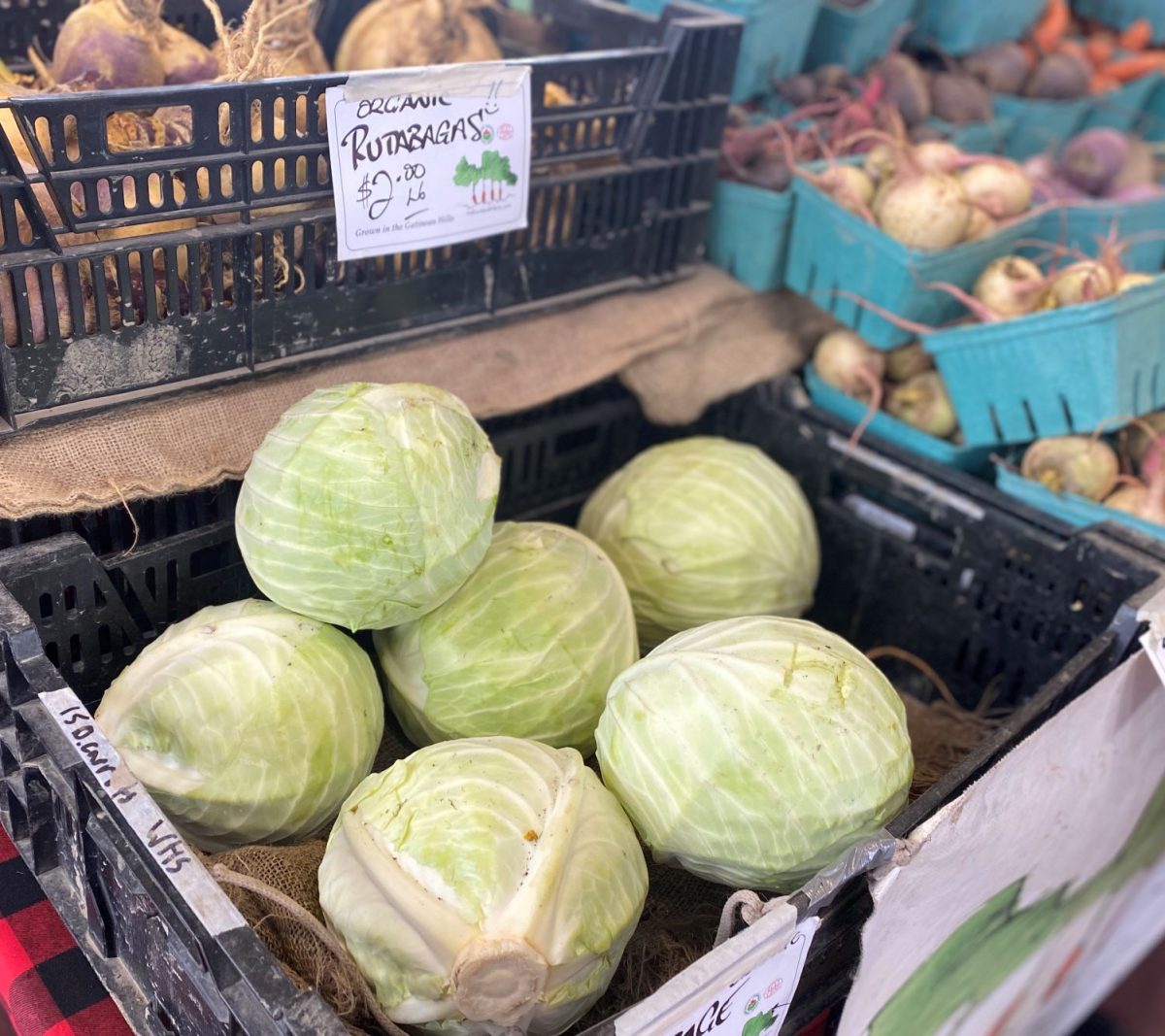 Baskets of cabbage, rutabagas, and other vegetables on a table at a farmers' market.