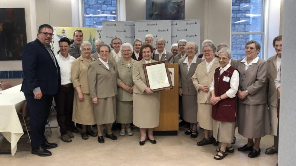 Guy Chartrand, Catherine McKenny, Mathieu Fleury, and the Sisters of Charity of Ottawa standing together at a podium in the cafeteria of a hospital.