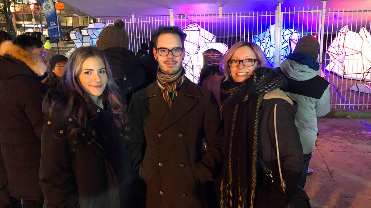 The bystanders smiling and standing in front of the art installation. 
Two girls and one guy from Montreal are in the photo. 