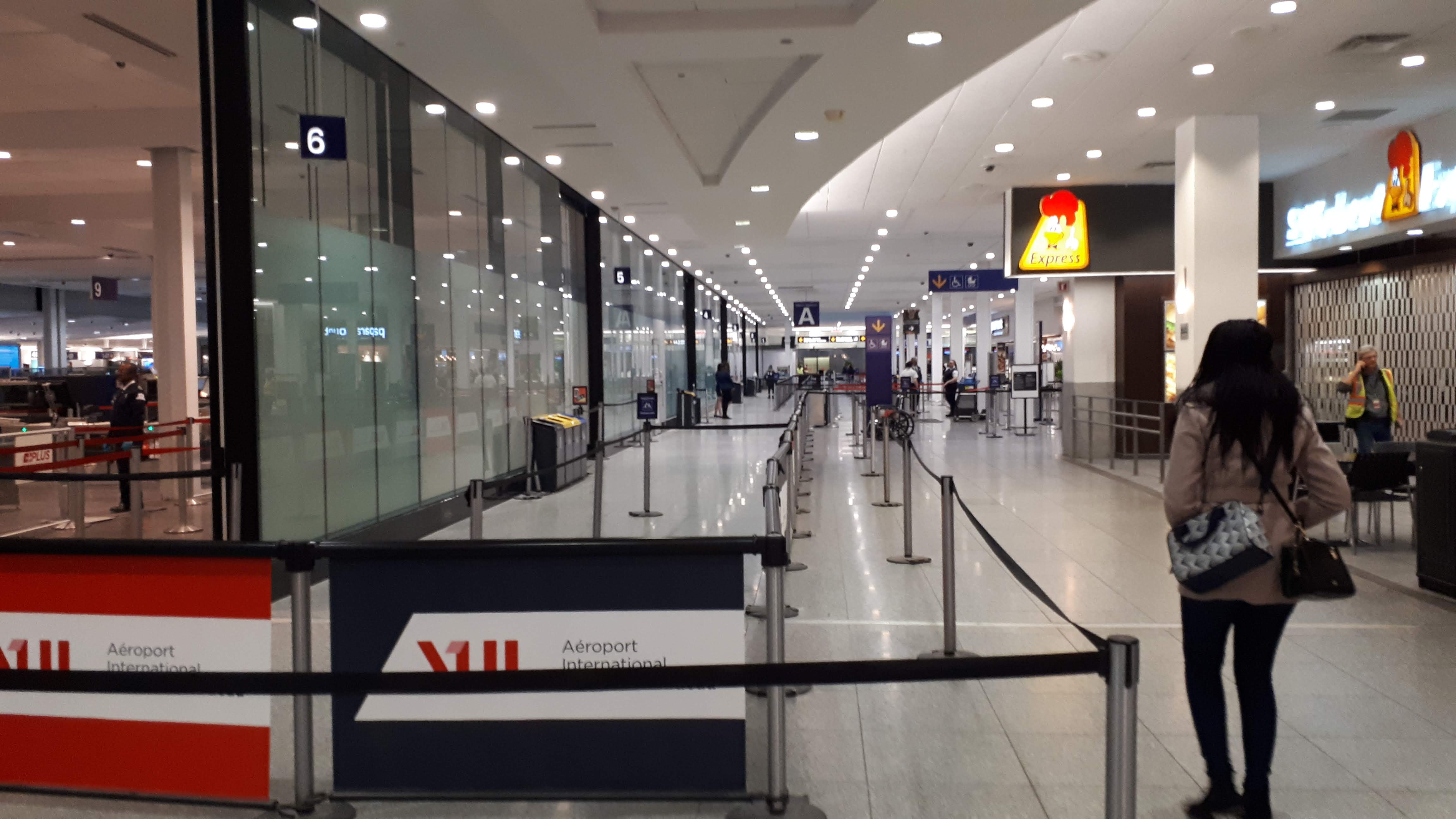 Barriers to create lines seen from left to right in image. One woman stands outside the barriers. No one can be seen within the stanchions besides a security official.