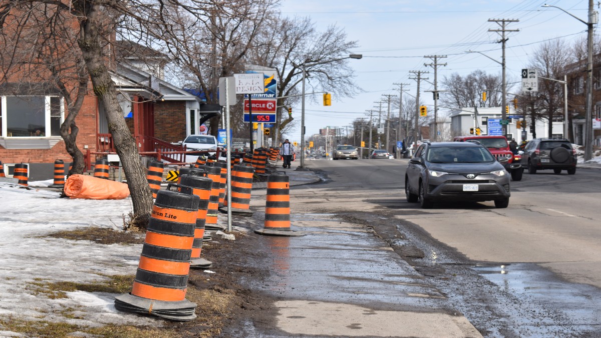 Construction cones placed along the sidewalk on the left side of Montreal Road. A car is driving by.