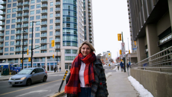 Liza Odokiienko poses on the sidewalk behind a busy street with apartment buildings in the background.