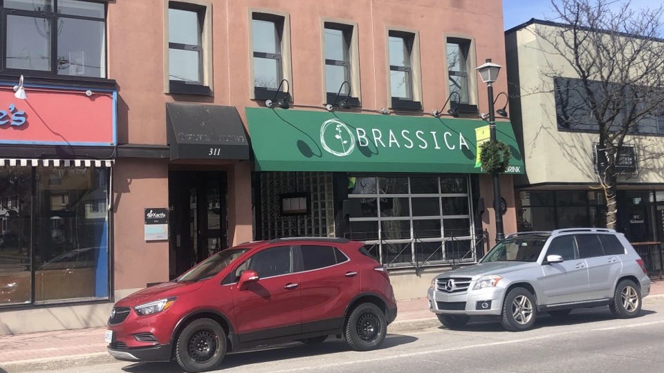 Sunny day. Cars parked in front of red building. Green Brassica sign.