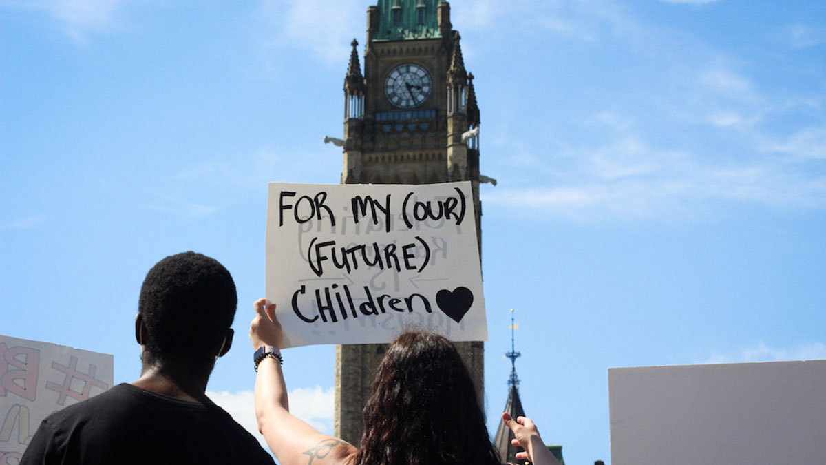 One woman holds a sign that says, “For my (our) (future) children" with the parliament building in the background.