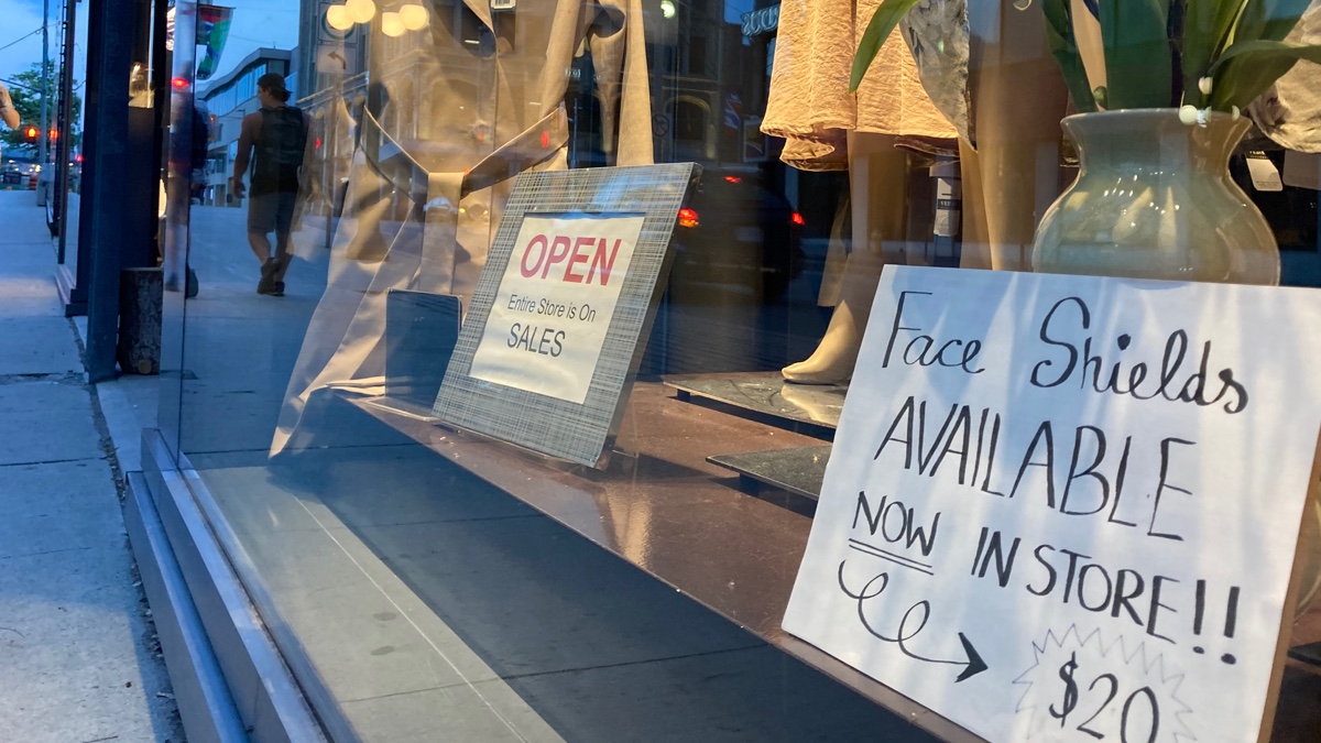 Store front window in a high-end fashion store with a sign saying "Face shields available. Now in store!!! $20"