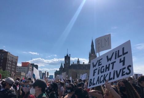 Protestors in masks hold signs in support of Black Lives Matter movement on Parliament Hill.