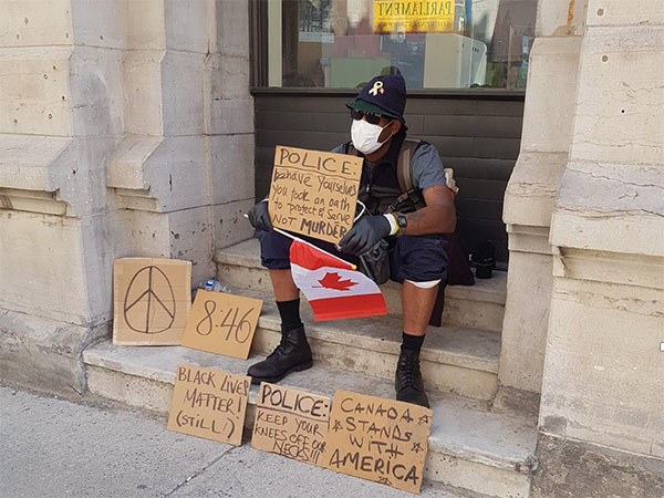 A man sits on steps with protest signs and a Canadian flag.