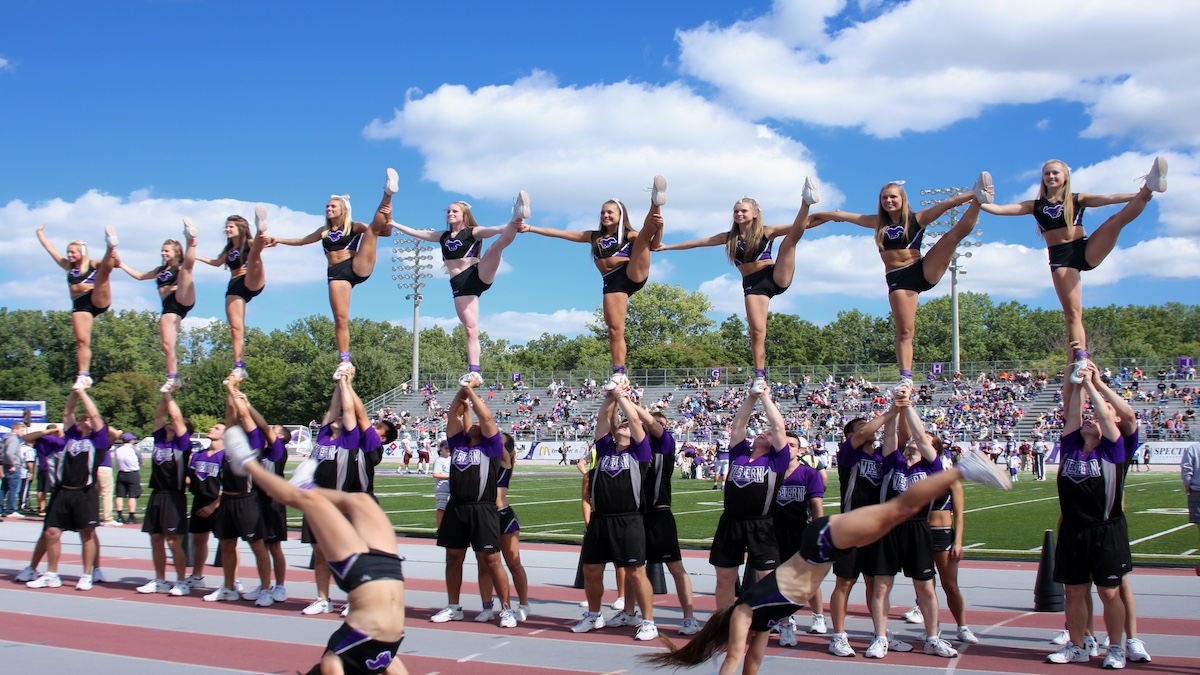 Cheerleaders perform stunts and tumbles at a football game.