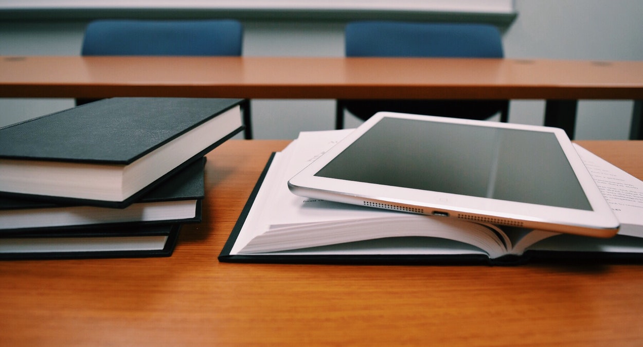 A picture of a stack of books and a tablet computer on top of an open book.