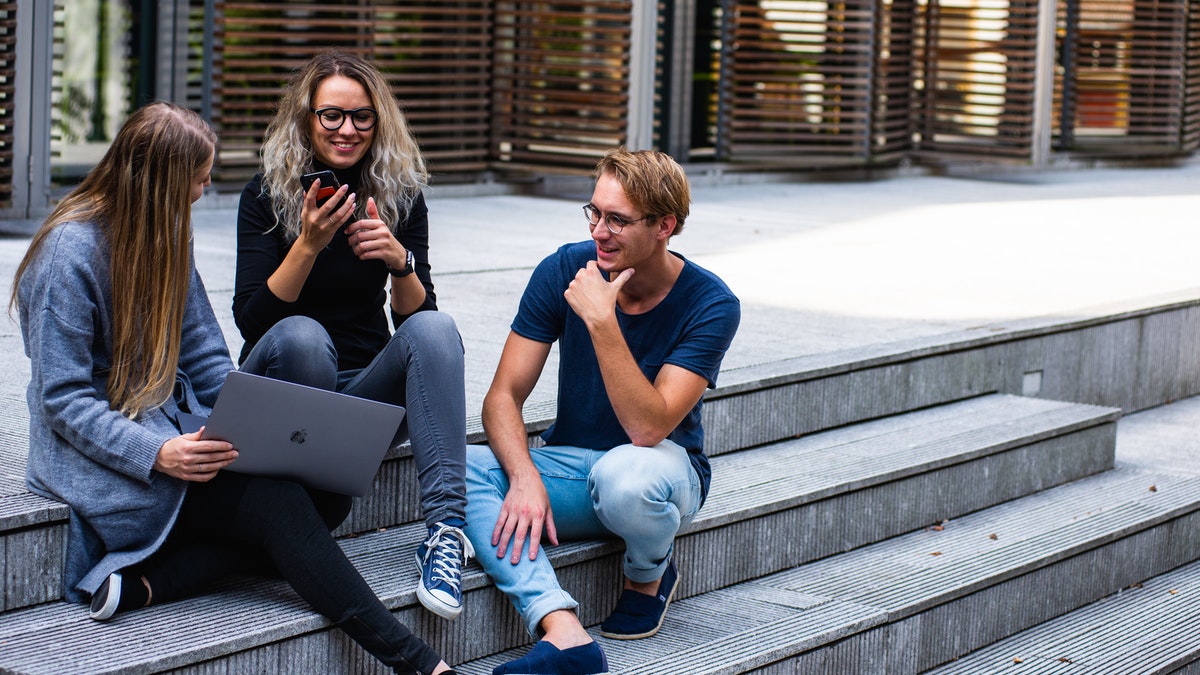 Three people sitting on outdoor stairs together, laughing.