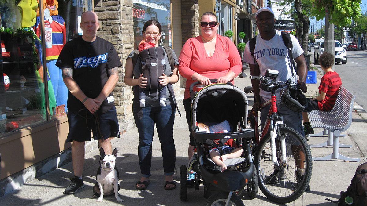 Four people, a baby, and a dog, stand on a street in Hamilton.