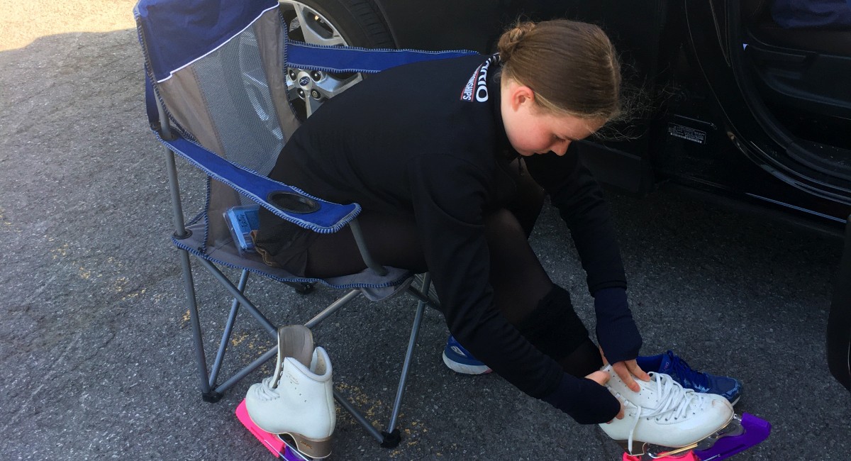 Picture of a figure skater tying up her skates in a parking lot because of COVID-19