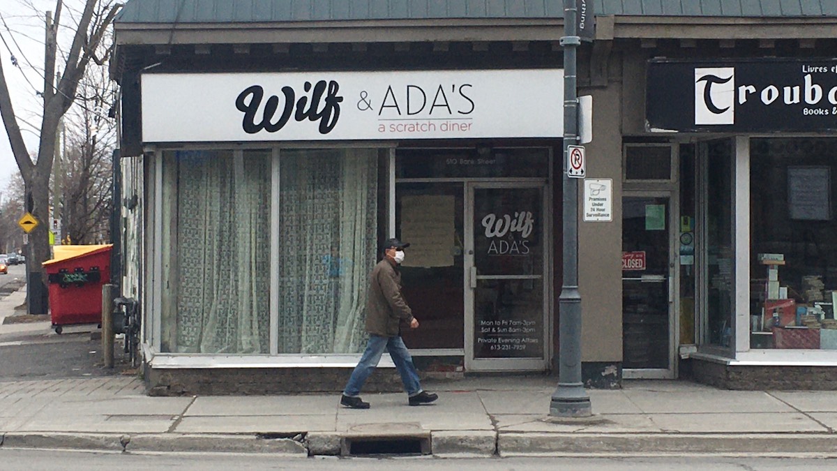 A man wearing a mask walks by Wilf & Ada's.