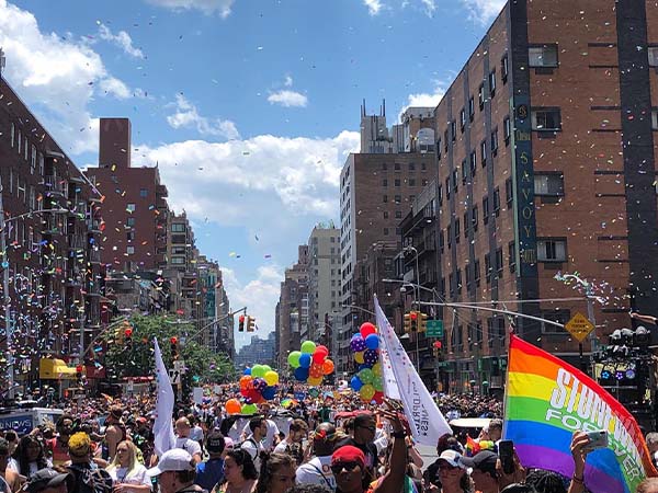 A large group of people in the street holding flags and balloons, while confetti is being thrown in the air.