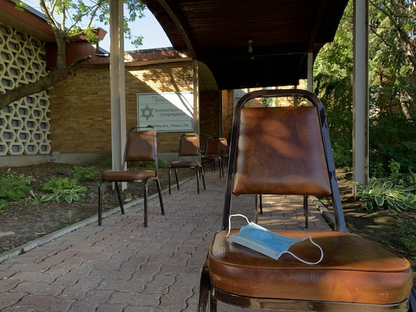 Socially-distanced chairs outside of Kehillat Beth Israel, with the KBI sign in the background. A mask is laid out on one of the spaced out chairs.