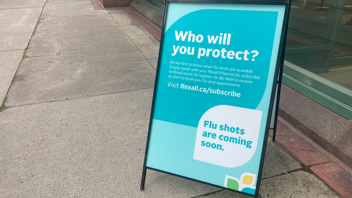 A sign outside a pharmacy that is promoting flu shots and reads "Who will you protect?"