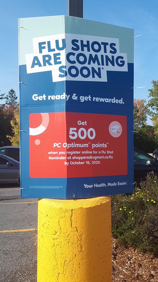 A sign in a parking lot that reads "flu shots are coming soon".