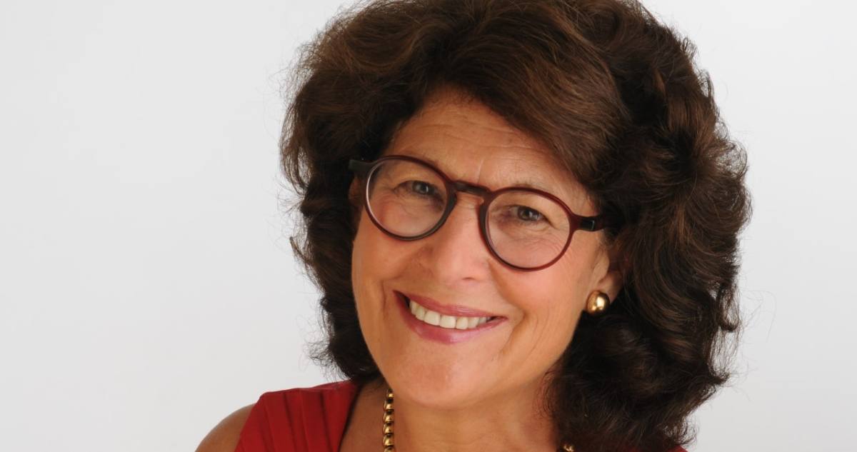 Woman with curly hair and glasses smiling into the camera against a white backdrop