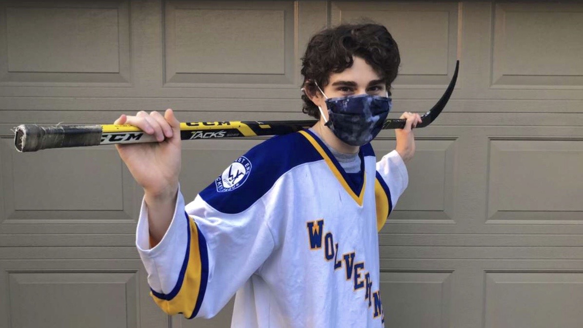 Danny Gaudet stands with his hockey stick and his face mask on.