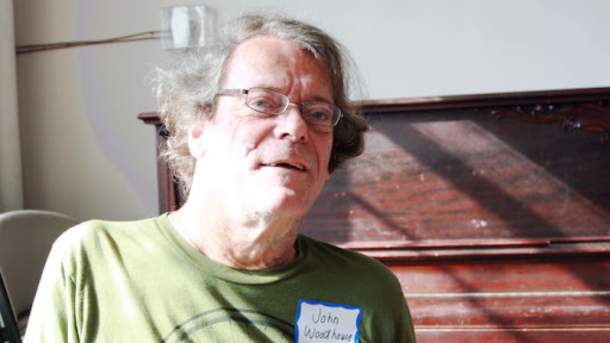 Close-up photo of John Woodhouse wearing a green shirt, glasses, and a nametag.