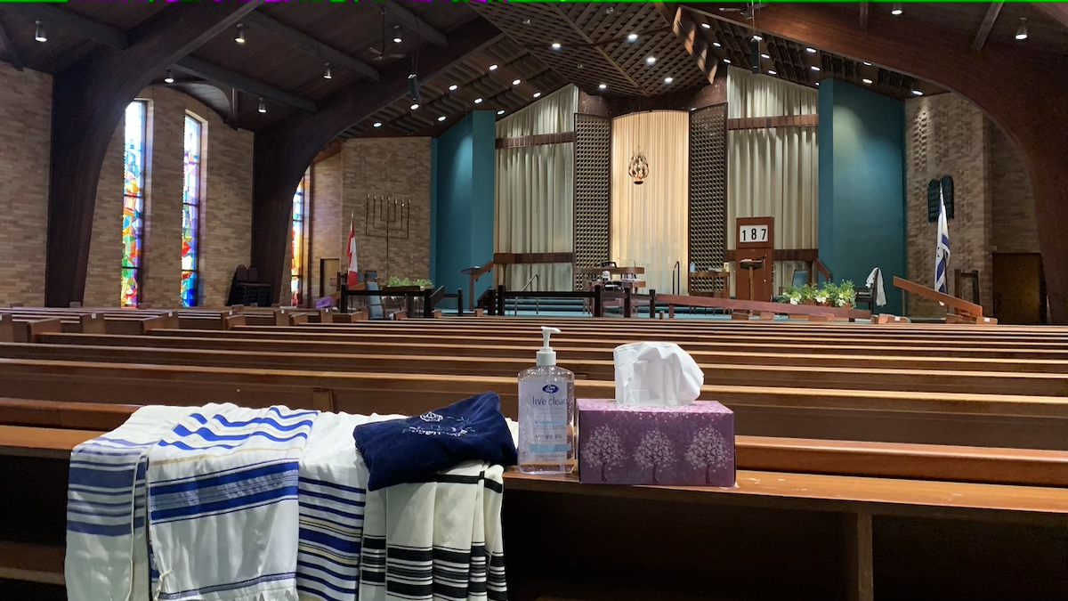 Prayer shawls drawn over empty pews alongside a tissue box and hand sanitizer at Kehillat Beth Israel synagogue.